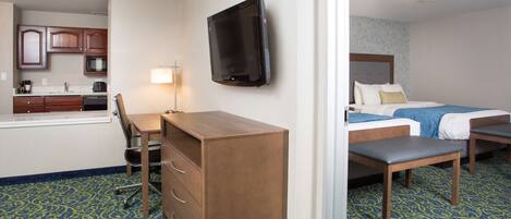 A hotel room with a kitchenette, a bed, a desk, and a television.