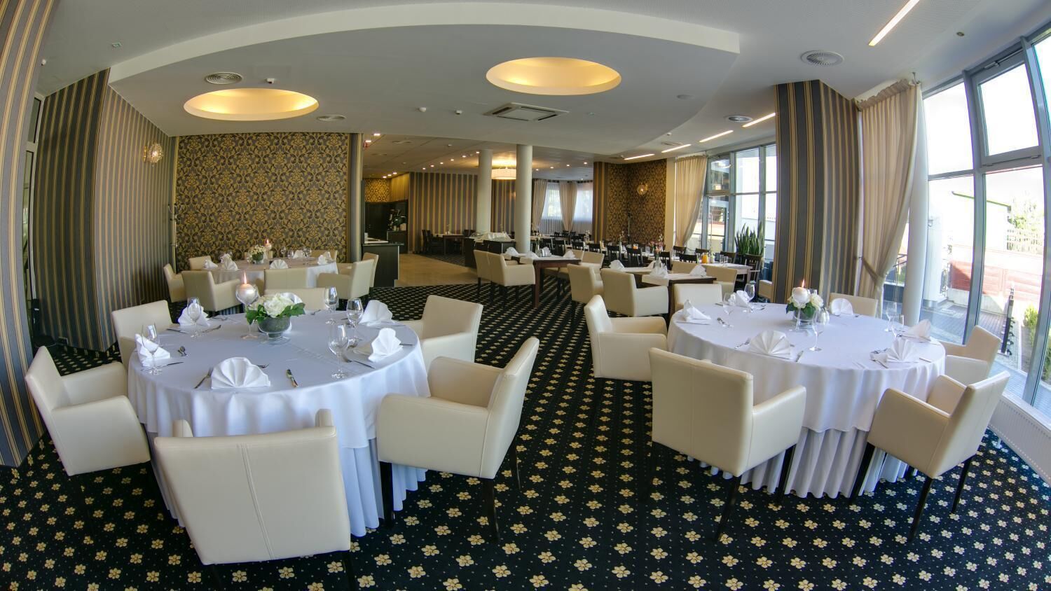 A hotel dining area with round tables set for dining, featuring white tablecloths and chairs.