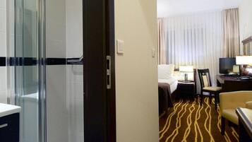 Habitación de hotel con ducha, cama, escritorio con computadora y televisor.