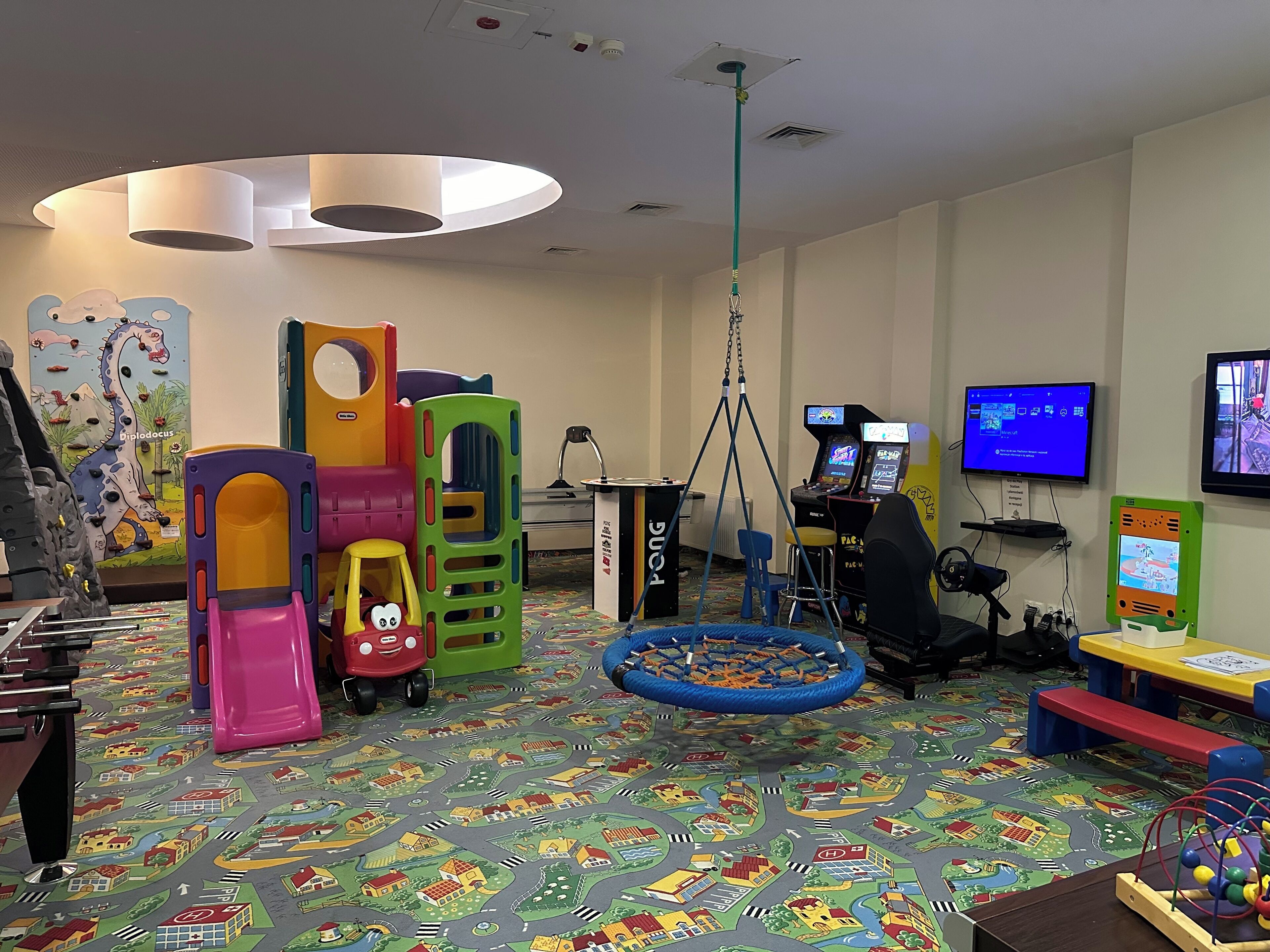 Un área de juegos infantiles con estructuras coloridas, una mesa de ping pong y juegos de arcade.