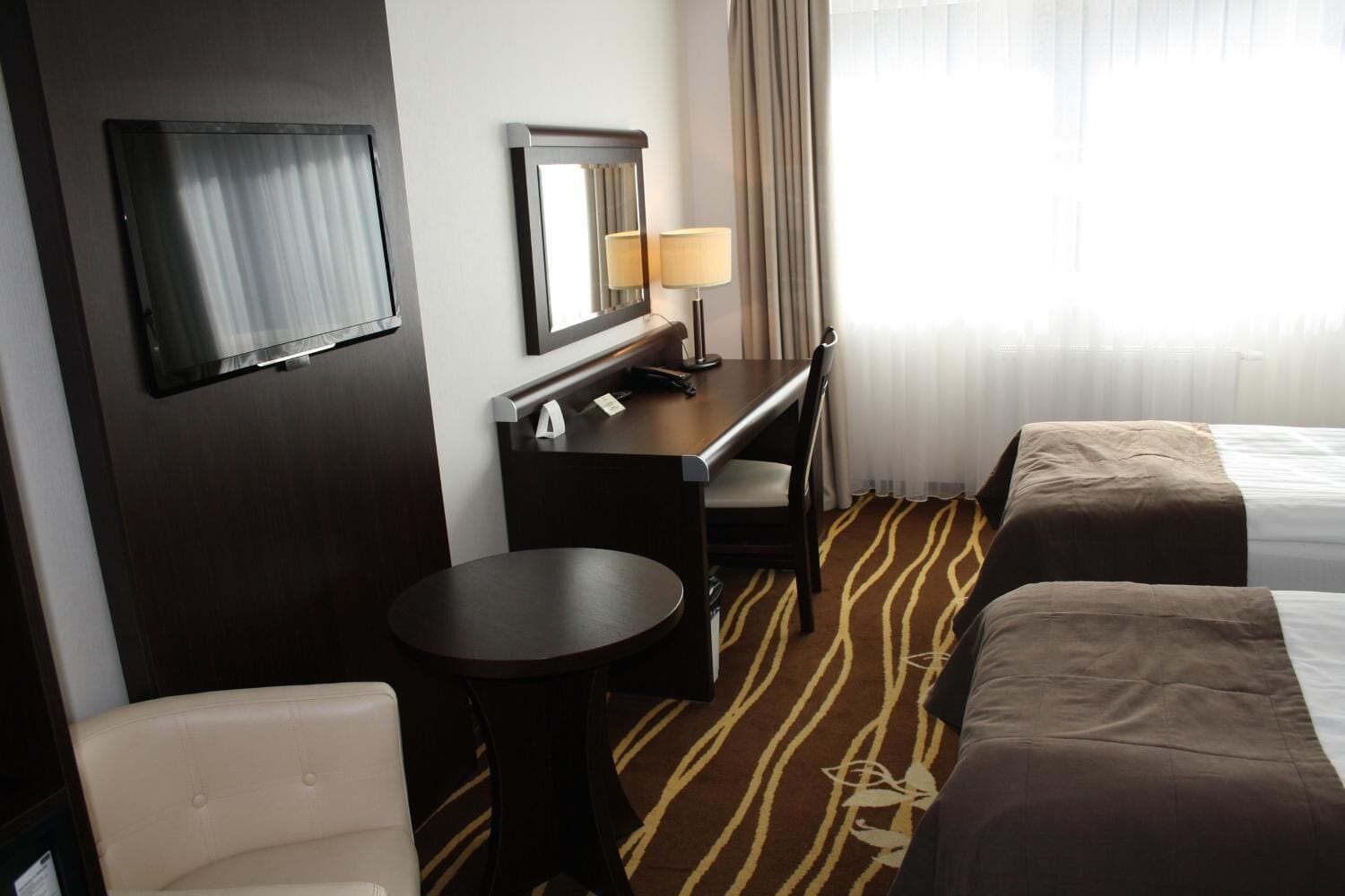 Une chambre d’hôtel avec un lit, un bureau, une chaise, une télévision et une lampe.