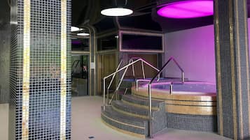 A modern spa area with a hot tub, a staircase, and a glass wall.