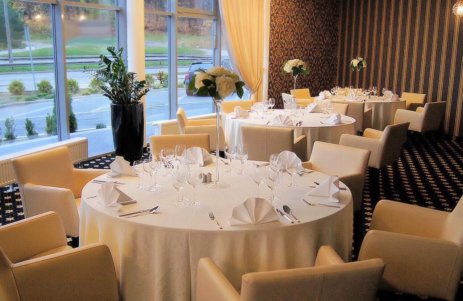 Ein Restaurant mit runden Tischen, großen Fenstern und Blick ins Freie.