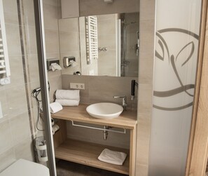 Une salle de bain moderne avec une douche à parois de verre, un meuble-lavabo en bois avec un lavabo blanc et un miroir au-dessus du lavabo.