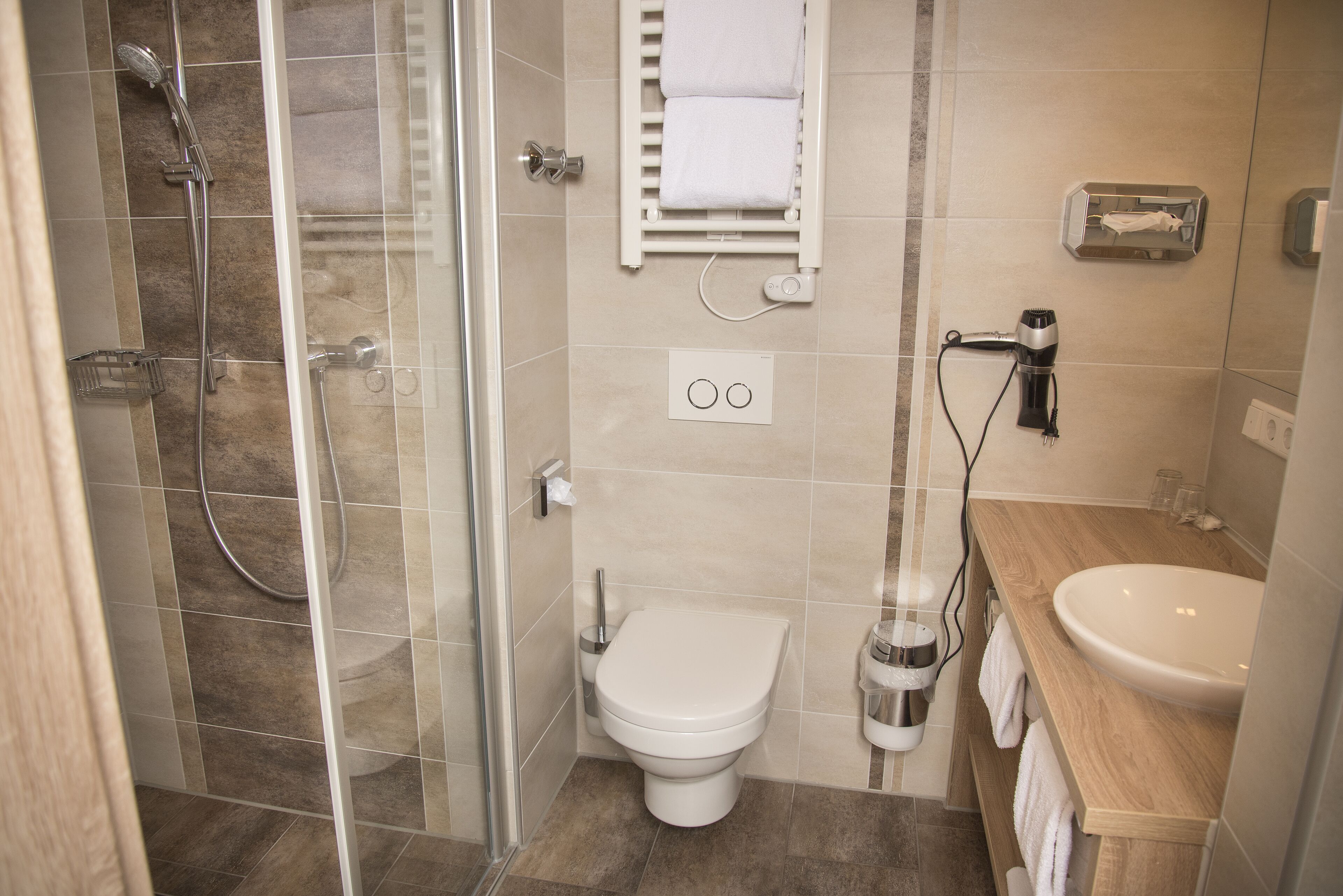 A modern bathroom with a glass shower enclosure, a white toilet, and a wooden vanity with a sink.