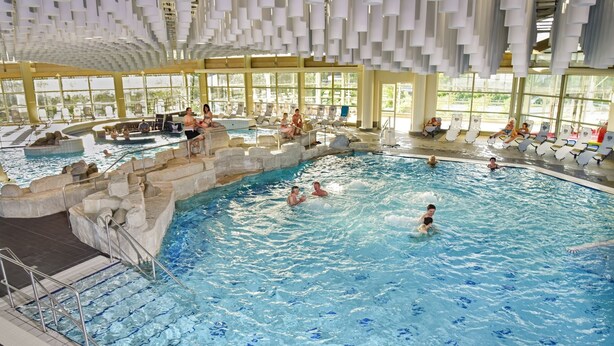 An indoor swimming pool with multiple lanes, stone steps, and a sunlit area with lounge chairs.