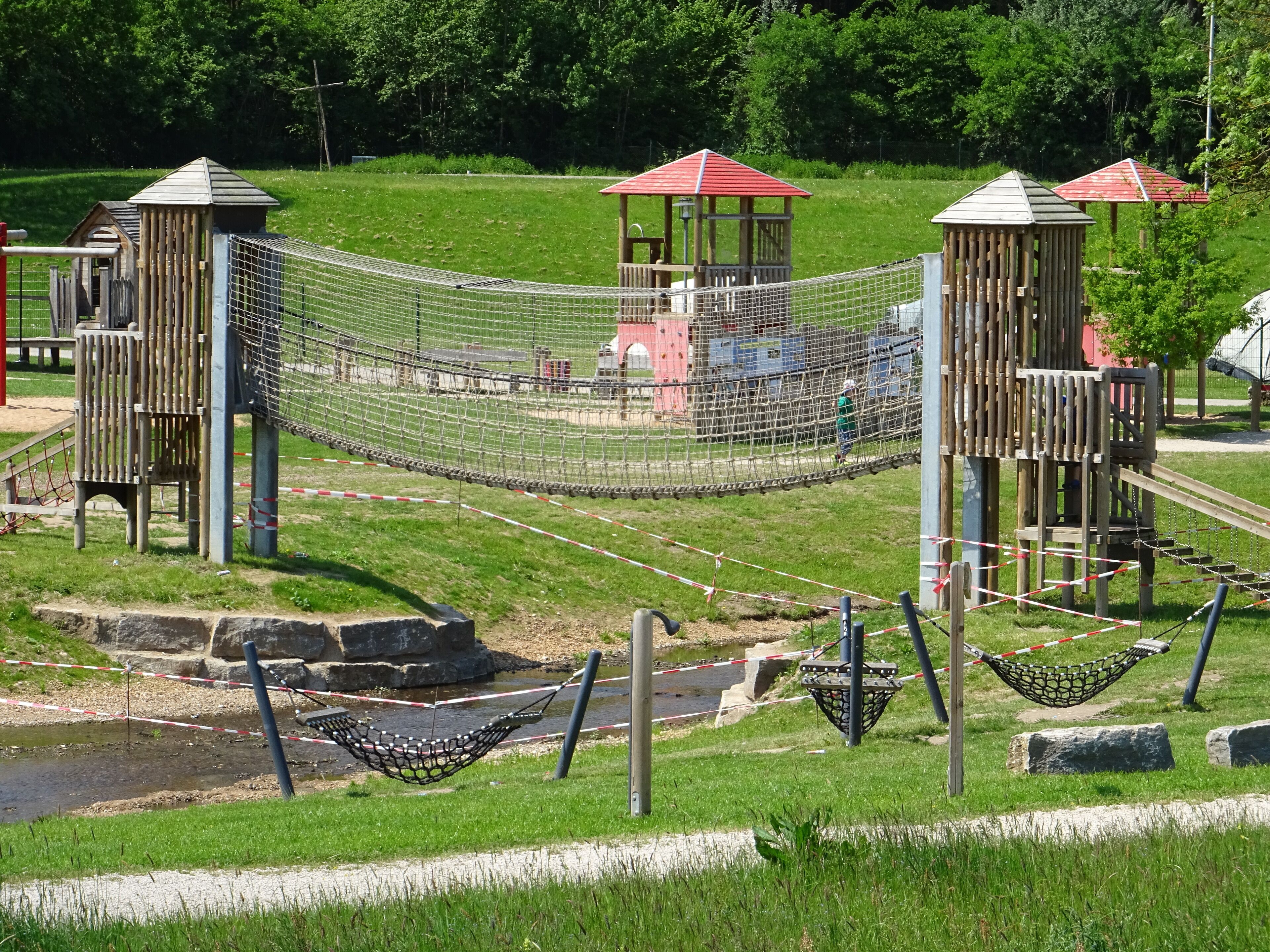 Ein Spielplatz mit Seilbrücken, Schaukeln und einem kleinen Wasserspiel.