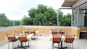 Un área de comedor en la azotea con mesas y sillas, rodeada de vegetación y un cielo despejado.