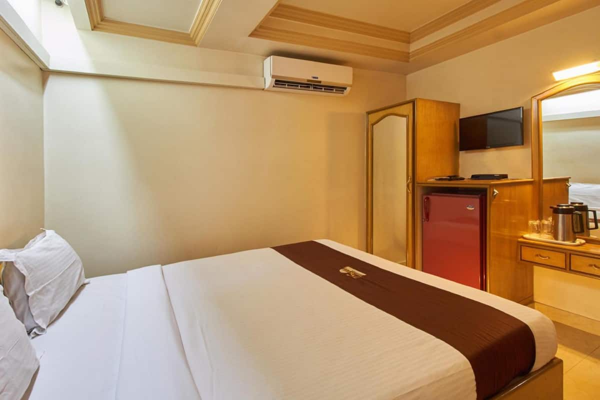 A hotel room with a bed, a TV, a wardrobe, a mirror, and a coffee maker.