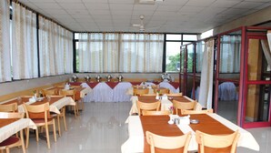 Un salón de conferencias con varias mesas y sillas, ventanas amplias con cortinas y una puerta de vidrio.
