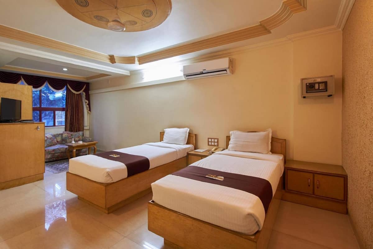 A hotel room with two single beds, a TV, an air conditioning unit, a desk, and a sofa.