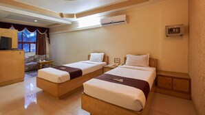 Habitación de hotel con dos camas individuales, televisión, aire acondicionado, escritorio y sofá.