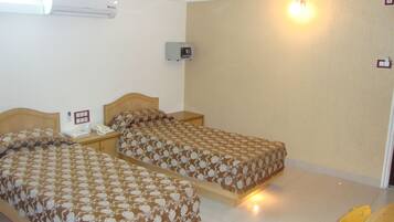 Habitación de hotel con dos camas, una mesita de noche con lámpara, un calentador de pared y un televisor pequeño.