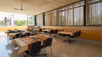 A conference room with multiple tables and chairs, large windows with patterned curtains, and a tiled floor.