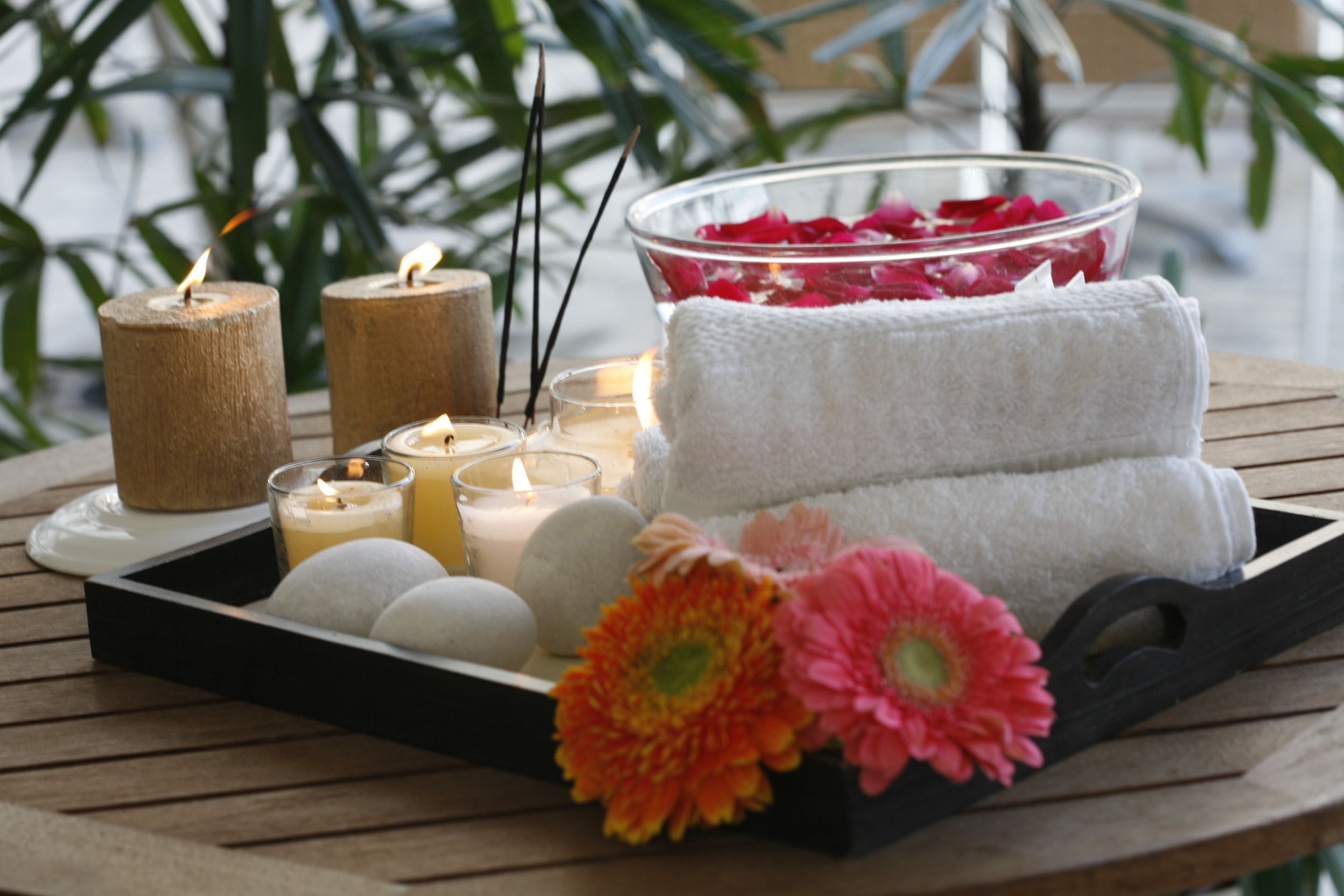 Una bandeja con velas, un cuenco de pétalos de rosa, toallas y flores sobre una mesa de madera.