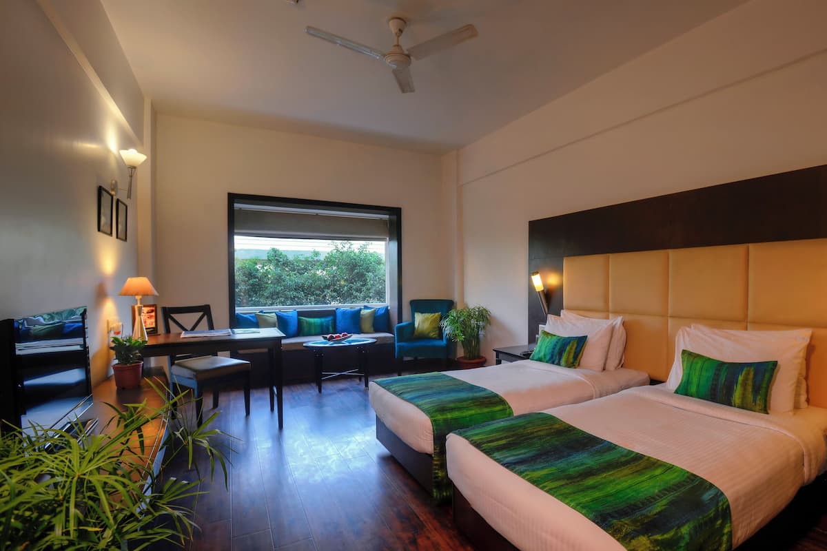 A hotel room with two beds, a sofa, a dining table, and a ceiling fan.