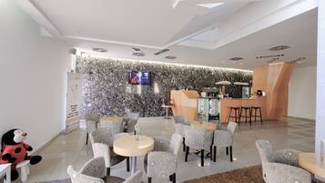 A modern hotel lobby with a reception desk, seating area, and a television screen.