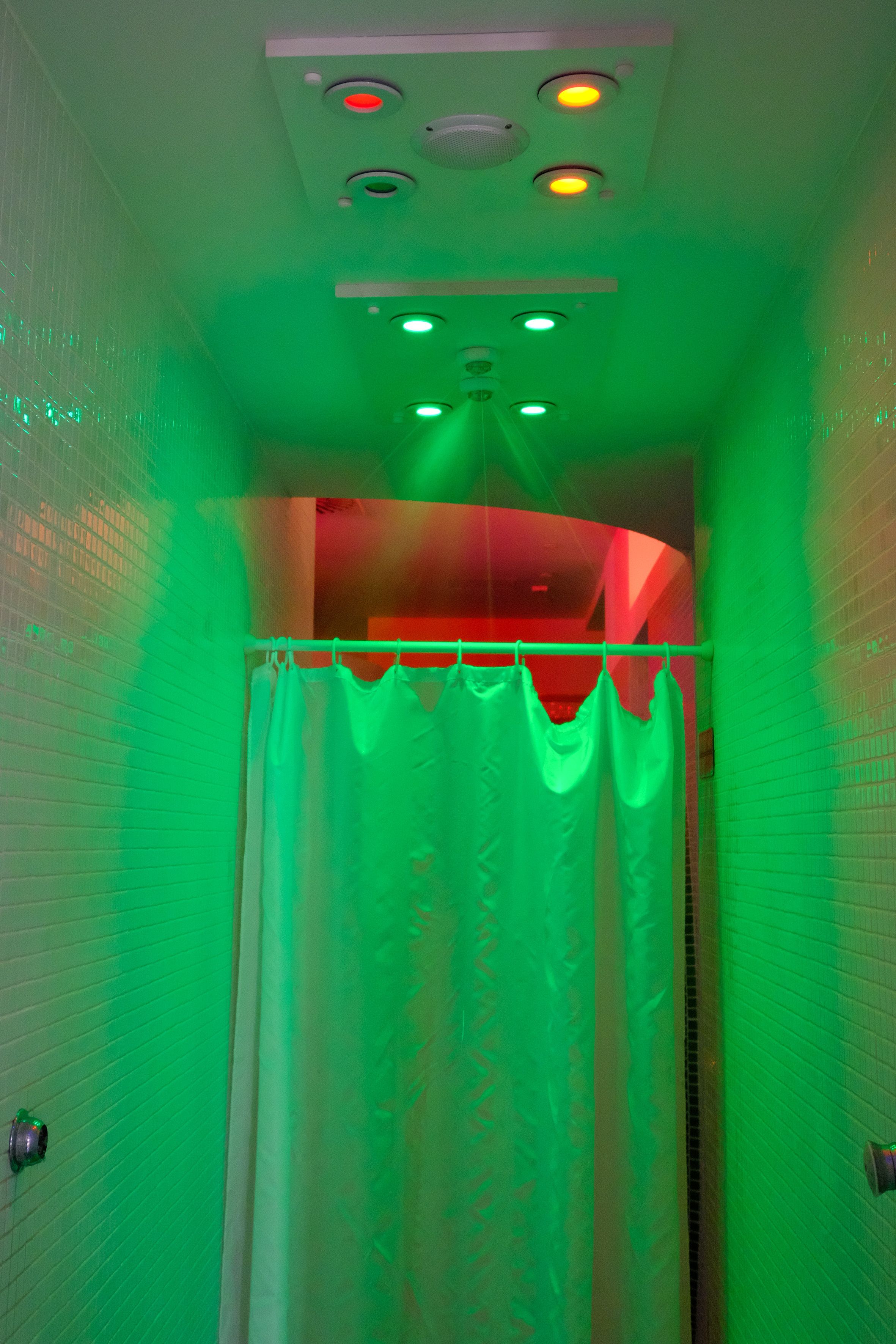 A bathroom with green lighting, a shower curtain, and a tiled wall.