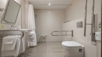 A modern bathroom with a toilet, a shower area, and a handrail.