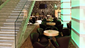 A modern interior with a glass staircase, seating area with round tables, and a stone wall with a flat-screen TV.