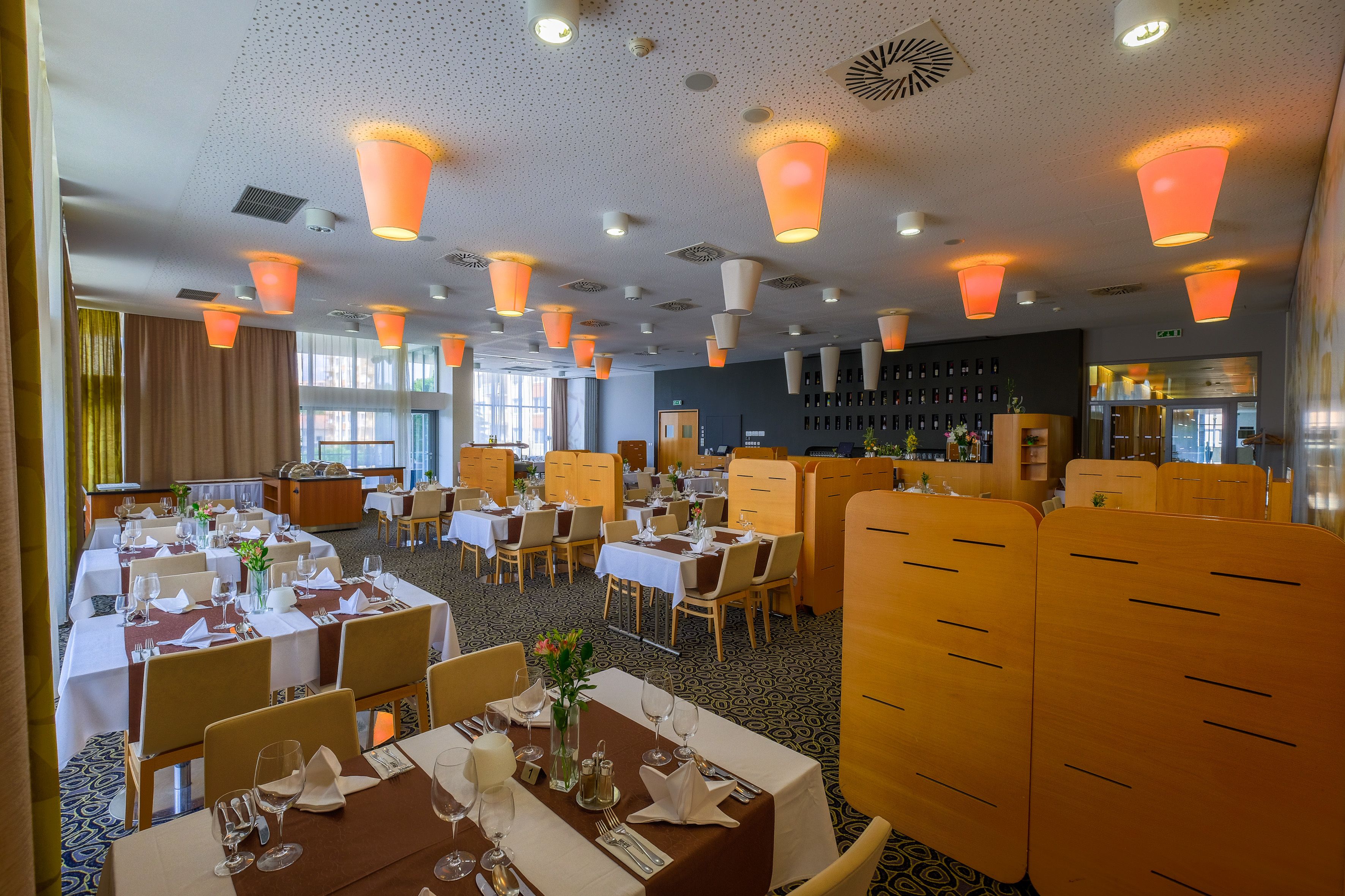 Un restaurant doté de plusieurs tables, recouvertes de nappes blanches et éclairées par des suspensions orange.