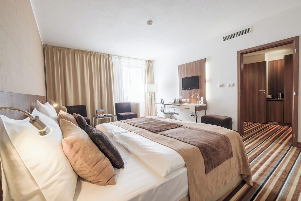 A hotel room with a bed, a desk, a chair, a TV, and a bathroom.