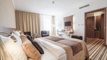 A hotel room with a bed, a desk, a chair, a TV, and a bathroom.