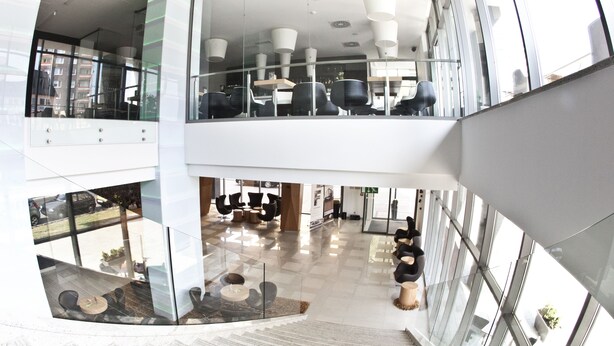 A modern interior with a glass atrium, a staircase, and seating areas.