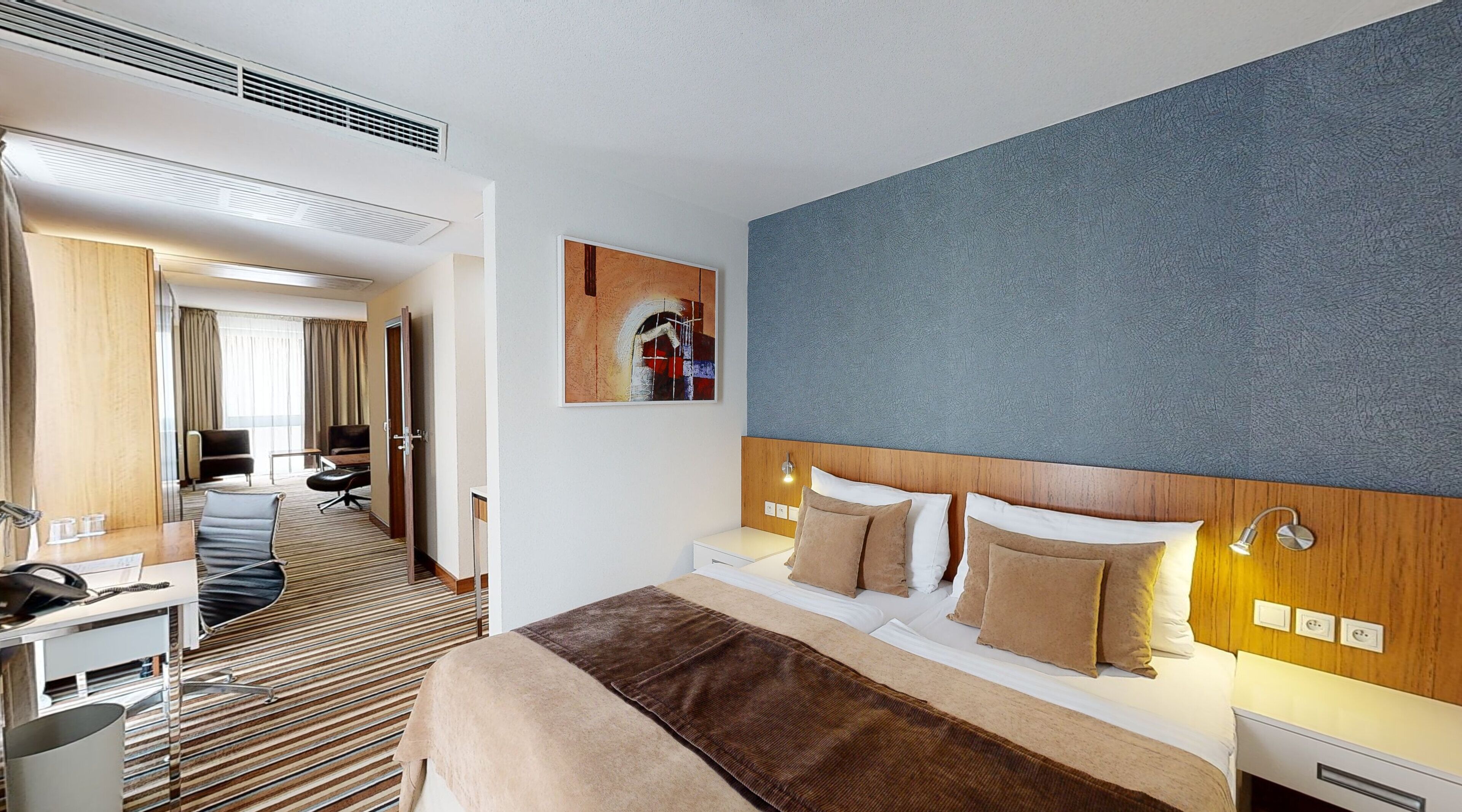 A hotel room with a large bed, a desk, a chair, and a view of the hallway.