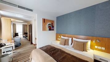 A hotel room with a large bed, a desk, a chair, and a view of the hallway.