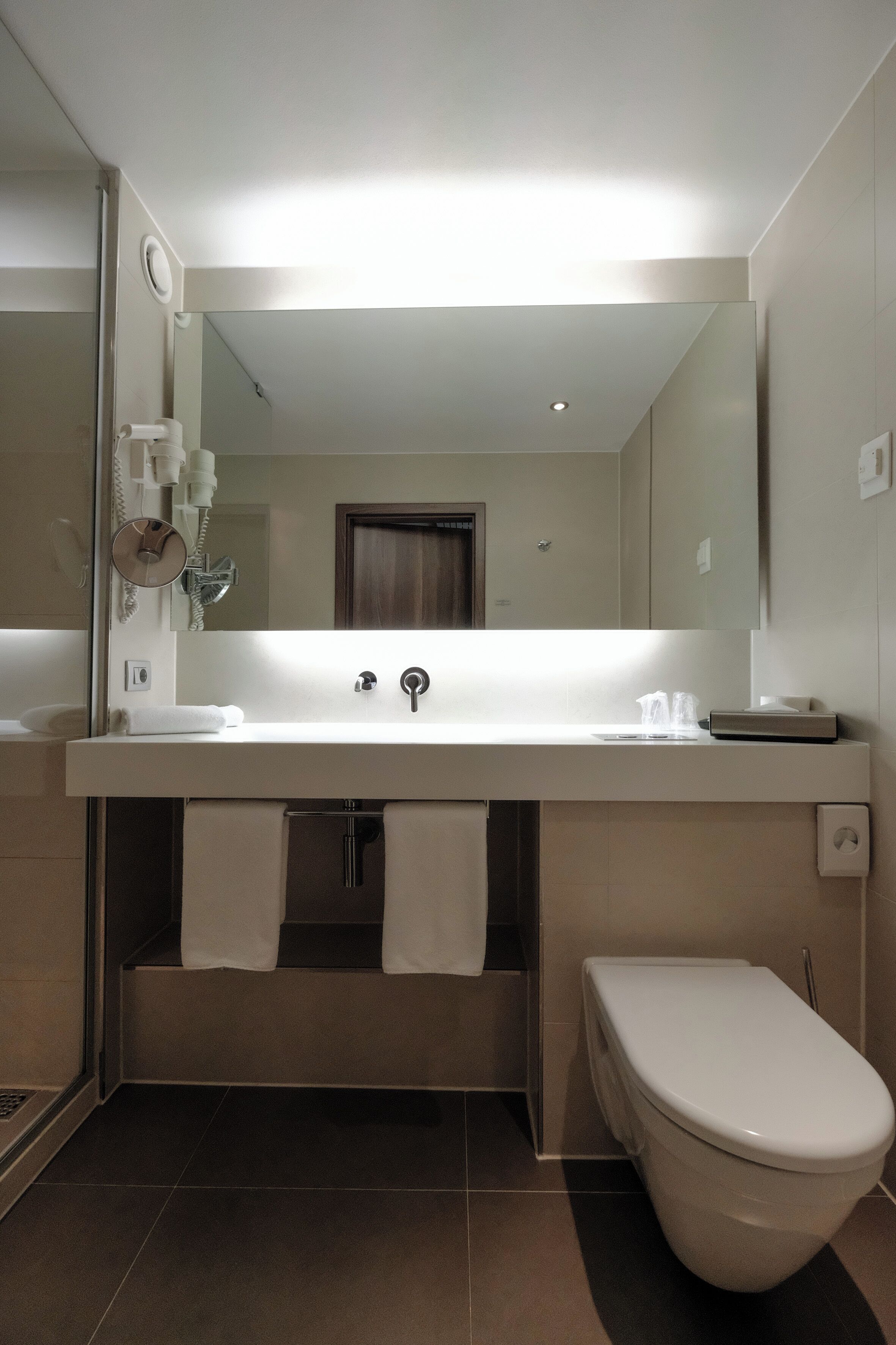 A modern bathroom with a white sink, a mirror above it, a toilet, and a shower area.
