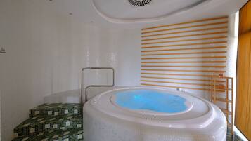 A modern bathroom with a large, round hot tub, a tiled shower area, and a wooden shelf with toiletries.