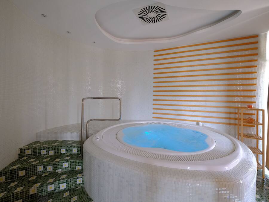 A modern bathroom with a large, round hot tub, a tiled shower area, and a wooden shelf with toiletries.