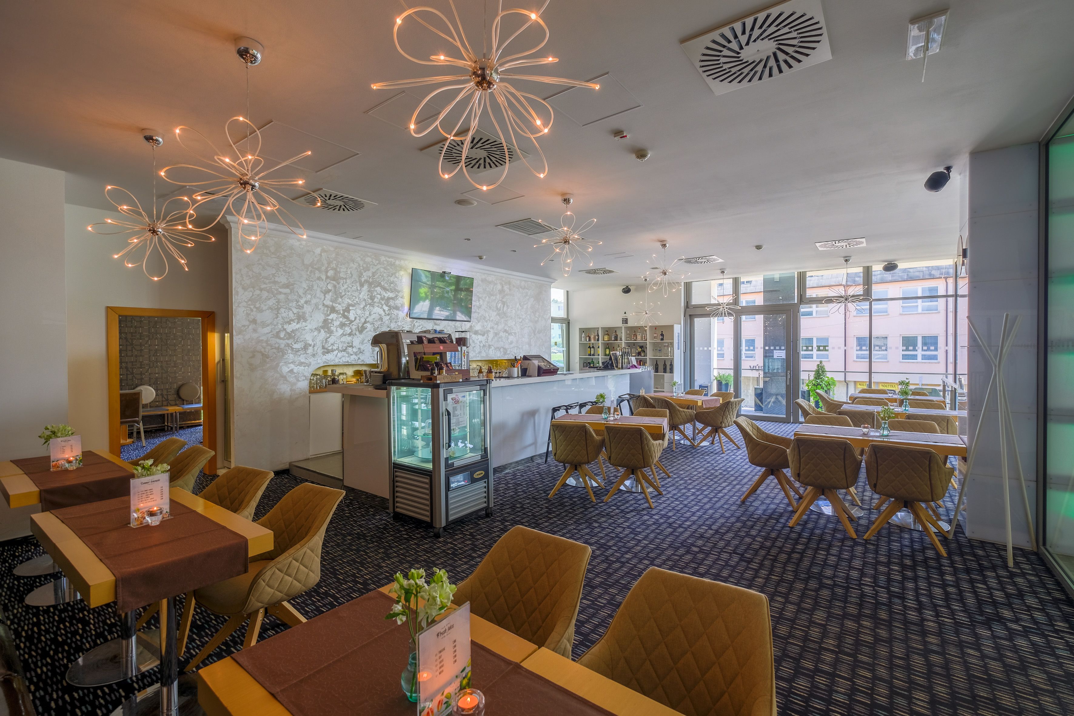 Un restaurant moderne doté de tables et de chaises, d’un bar et d’une grande fenêtre donnant sur la ville.