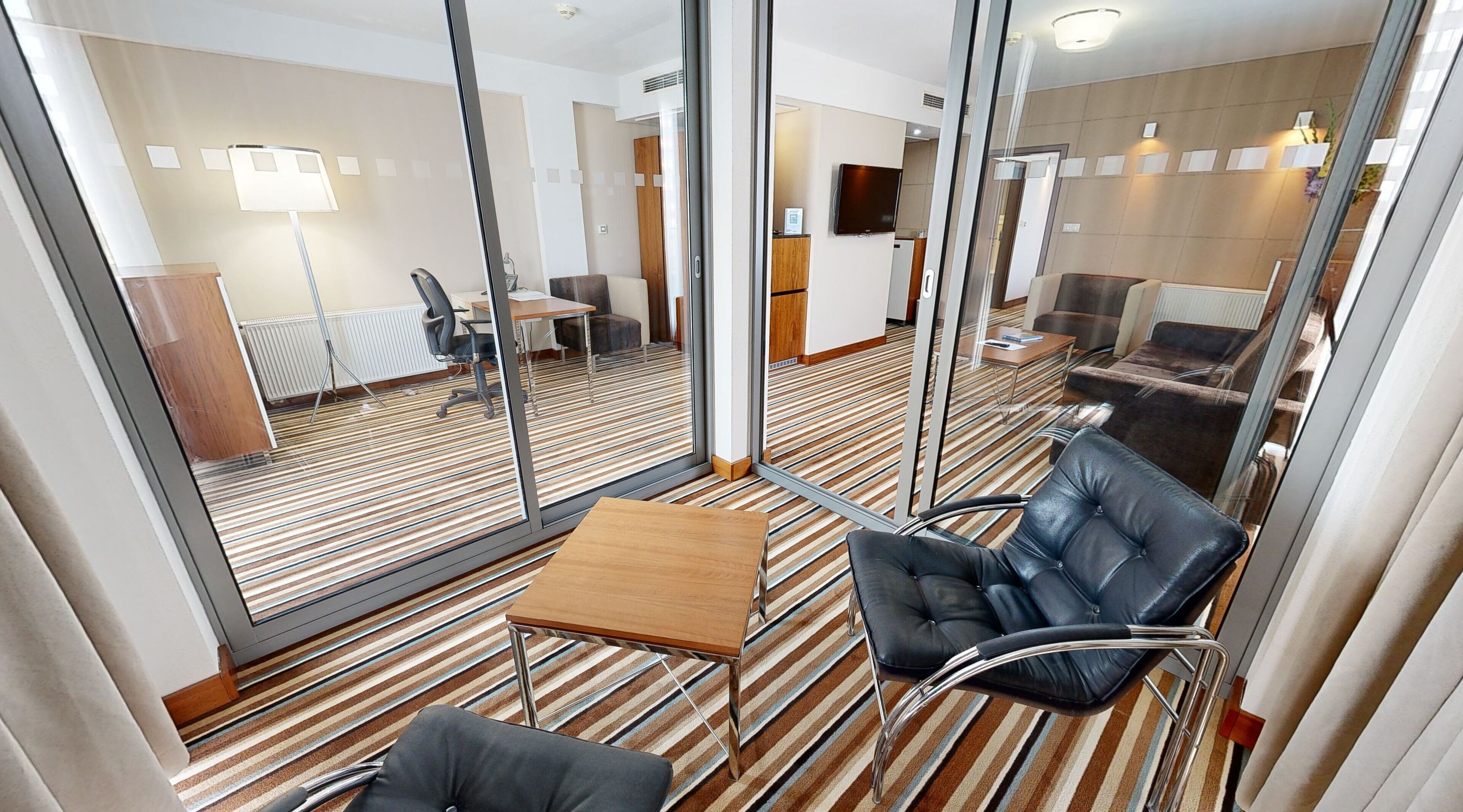 A hotel room with a large window, a wooden table, a leather chair, and a striped carpet.