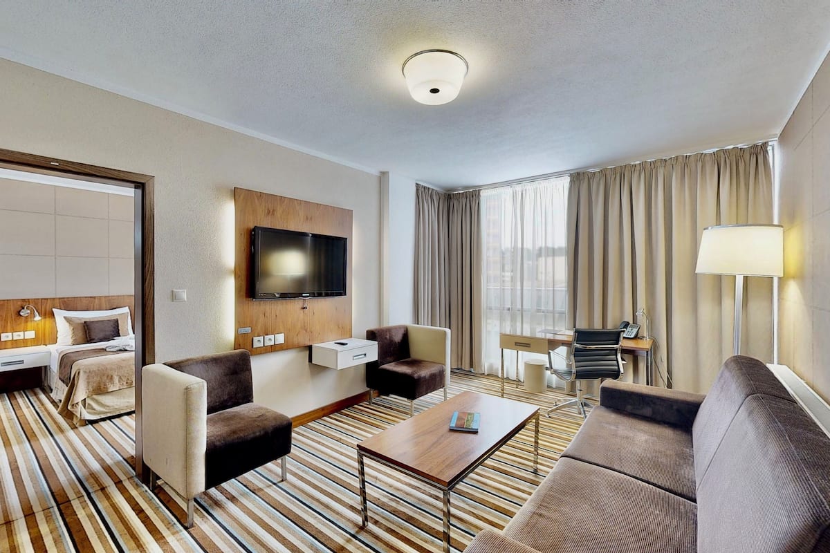 A hotel room with a bed, a TV, a desk, a chair, a sofa, and a coffee table.