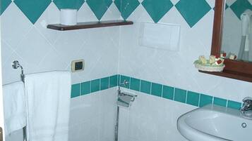 A bathroom with a toilet, bidet, and sink, featuring a green and white tile pattern.