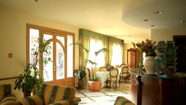 A spacious living room with a large window, a dining area, and a reception desk. - Hotel Ristorante Stella 2000 (Olbia)