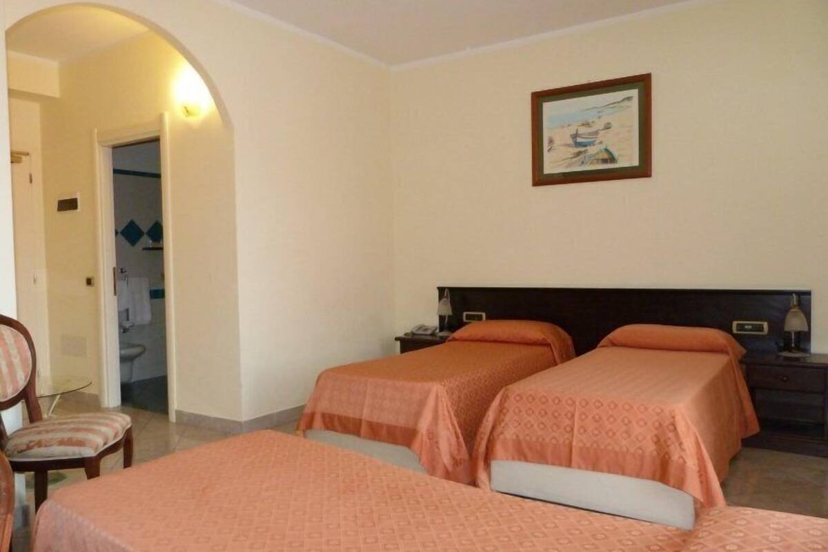 A hotel room with two beds, a chair, a desk, and a painting on the wall.