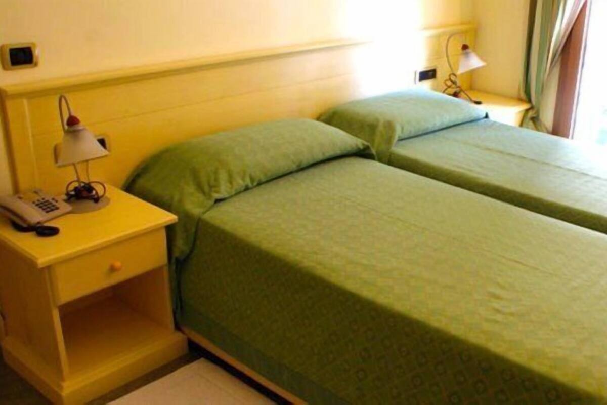A hotel room with two single beds, a nightstand with a lamp, a telephone, and a window with curtains.
