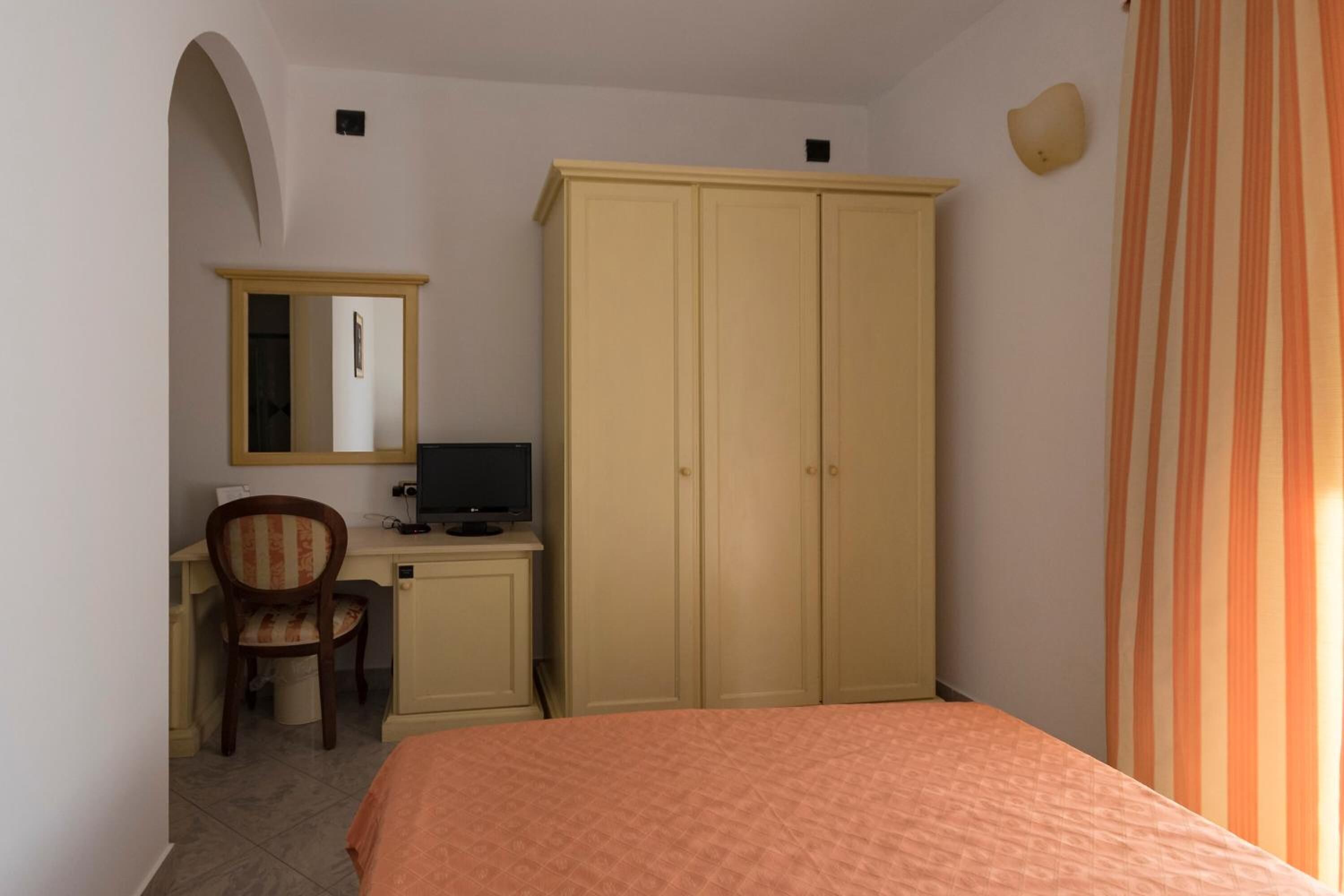 A bedroom with a bed, a desk with a computer, a chair, and a wardrobe.