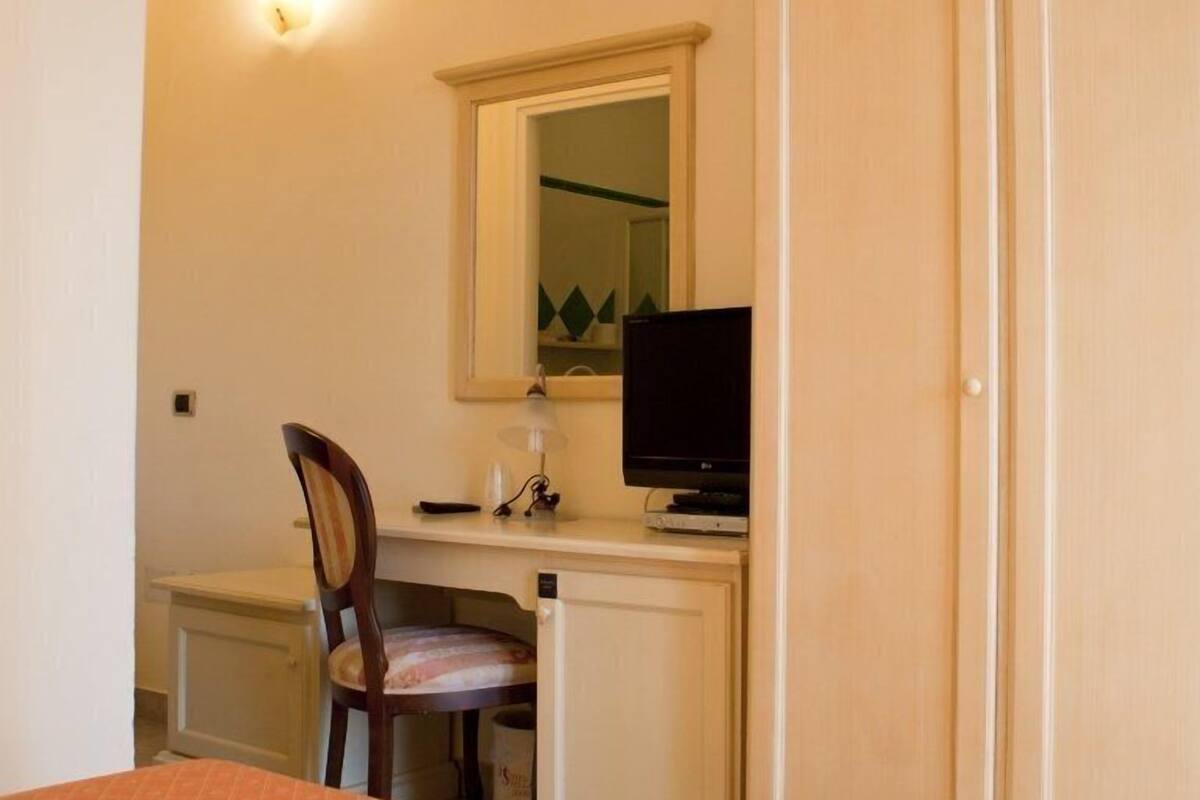 A small room with a desk, chair, television, and a mirror.