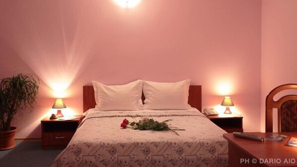 A hotel room with a bed, two bedside lamps, a nightstand, a potted plant, and a chair.