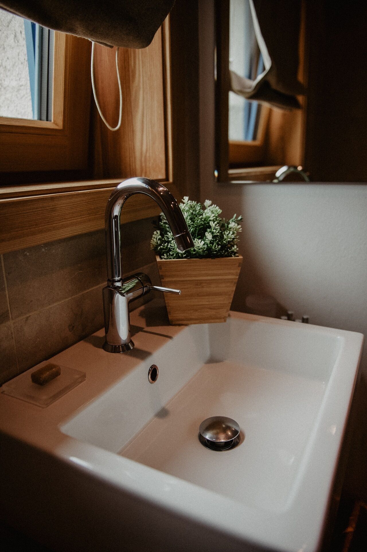 A bathroom sink with a modern faucet, a wooden planter with greenery, and a mirror above the sink.