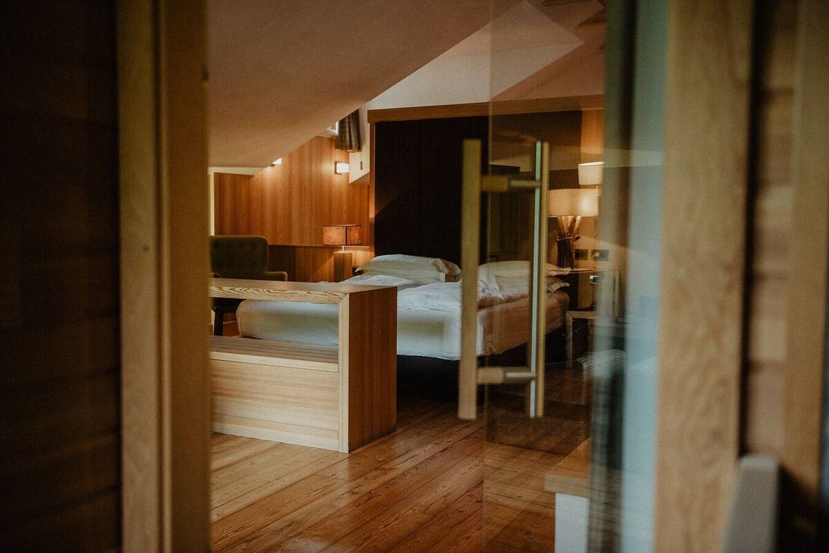 A compact hotel room with a bed, bedside table, lamp, and wooden flooring.