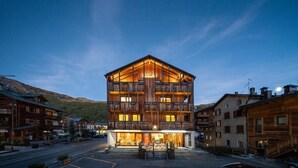 A multi-story hotel with a wooden facade, balconies, and a street view with other buildings.