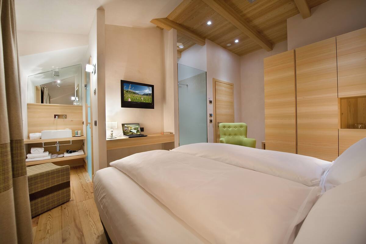 A modern bedroom with a large bed, a television, a wooden wardrobe, and a green armchair.