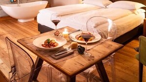 A modern hotel room with a large bed, a wooden table with a meal, and a bathtub.