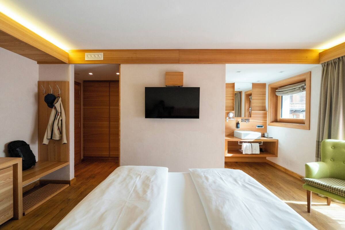 A hotel room with a bed, a TV, a bathroom with a sink and mirror, and a green chair.