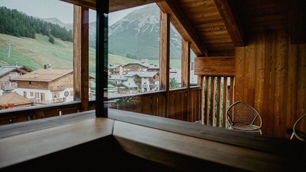 A wooden cabin with a balcony overlooking a mountain village.